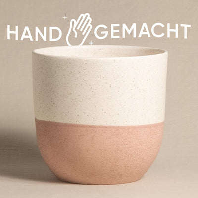 Ein schöner Keramik-Topf (Variado | 22 cm ⌀) mit einer gesprenkelten weißen oberen Hälfte und einer glatten Terrakotta-unteren Hälfte steht zentriert vor einem hellbraunen Hintergrund. Über dem Topf steht das Wort „HAND GEMACHT“ mit einem Handsymbol zwischen den Wörtern.