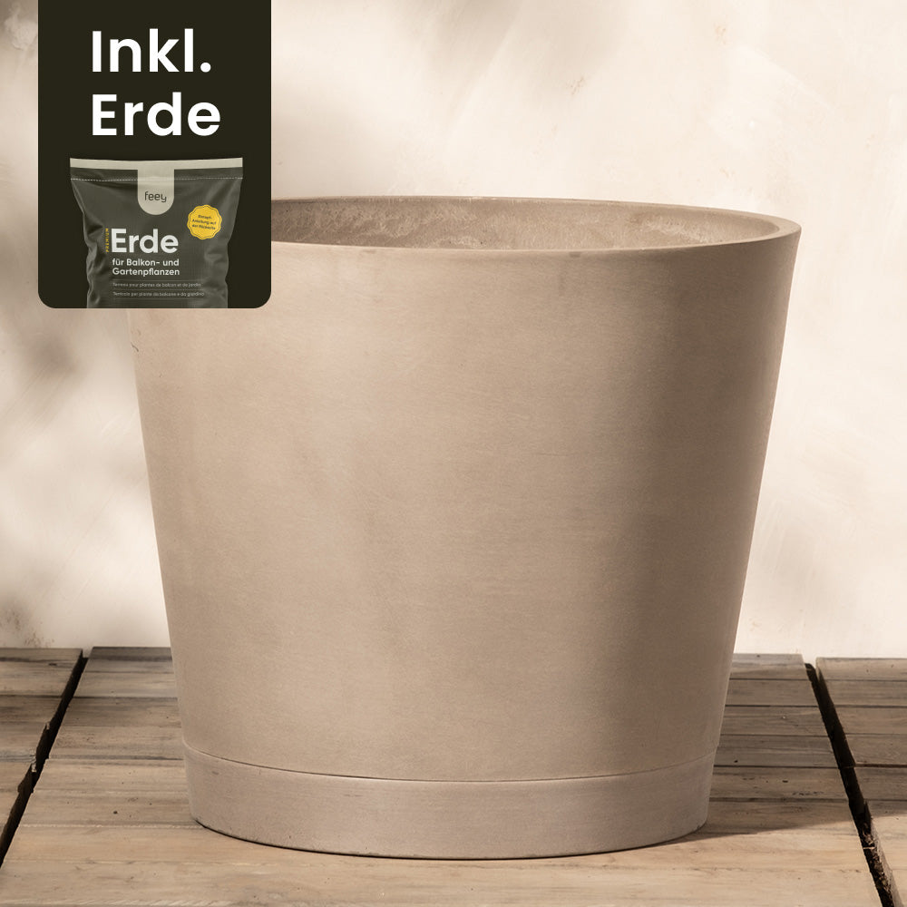 Ein großer, beiger, zylindrischer Pflanzkübel aus Kunststoff (Venedig | 40 cm ⌀) steht auf einem Holzboden vor einer hellen Wand. In der oberen linken Ecke ist ein kleineres Bild eines Sacks Erde mit dem Text „Inkl. Erde“ zu sehen, der darauf hinweist, dass der Topf mit Erde geliefert wird. Der Pflanzkübel aus Kunststoff (Venedig | 40 cm ⌀) verfügt außerdem über ein effizientes Drainage-System, das Staunässe verhindert.