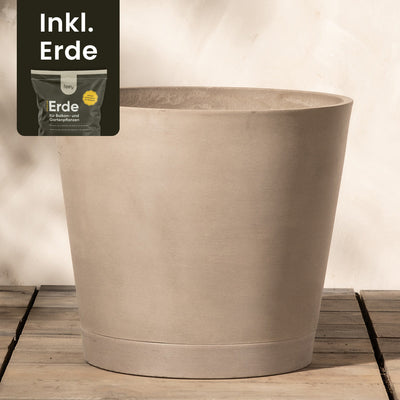 Ein großer, beiger, zylindrischer Pflanzkübel aus Kunststoff (Venedig | 40 cm ⌀) steht auf einem Holzboden vor einer hellen Wand. In der oberen linken Ecke ist ein kleineres Bild eines Sacks Erde mit dem Text „Inkl. Erde“ zu sehen, der darauf hinweist, dass der Topf mit Erde geliefert wird. Der Pflanzkübel aus Kunststoff (Venedig | 40 cm ⌀) verfügt außerdem über ein effizientes Drainage-System, das Staunässe verhindert.