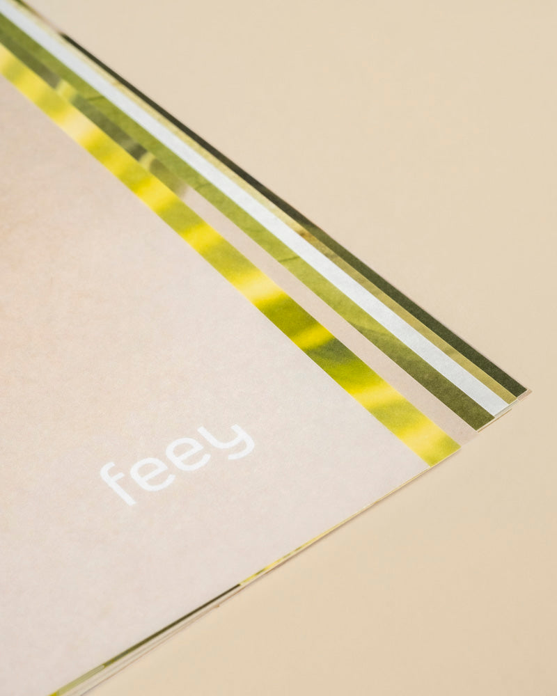 Nahaufnahme des Pflanzenkalenders mit aufgedrucktem "feey" und grün-gelb-weiß gestreiften Rändern - ideal als immerwährender Kalender oder Geschenk für Pflanzenfans - vor beigem Hintergrund.