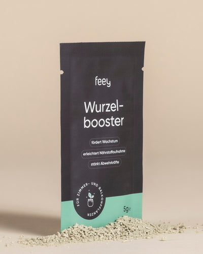Ein schwarz-grünes Wurzelbooster"-Paket steht aufrecht auf einer beigen Fläche mit hellbeigem Pulver drum herum. Die Verpackung hebt Trichoderma atrobunneum für verbessertes Pflanzenwachstum und Pflanzengesundheit in deutscher Sprache hervor.