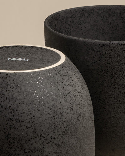 Nahaufnahme von zwei schwarzen Keramik-Töpfen (Direito | 25 cm ⌀); einer aufrecht mit offener Oberseite, der andere umgedreht mit "feey" auf dem Boden. Beide haben eine matte, gesprenkelte Oberfläche - ideal für die stilvolle Präsentation von Zimmerpflanzen.