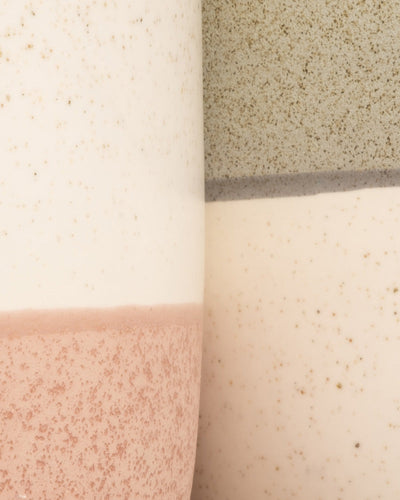 Eine Nahaufnahme von drei handgefertigten Keramikoberflächen mit einer gesprenkelten Textur in Creme, gedämpftem Rosa und Salbeigrün bildet eine abstrakte horizontale Komposition. Diese Stücke eignen sich ideal als Keramik-Topfset „Variado“ und haben eine matte Oberfläche.