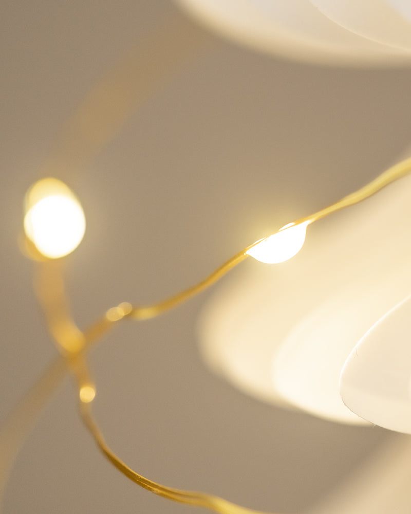 Eine Nahaufnahme einer warmweißen Lichterkette vor einem weichen, verschwommenen Hintergrund. Die Lichter leuchten, und der Draht sieht golden aus, er wölbt sich sanft über den Rahmen und schafft eine gemütliche und stimmungsvolle Atmosphäre, die perfekt für die Weihnachtsdekoration ist.