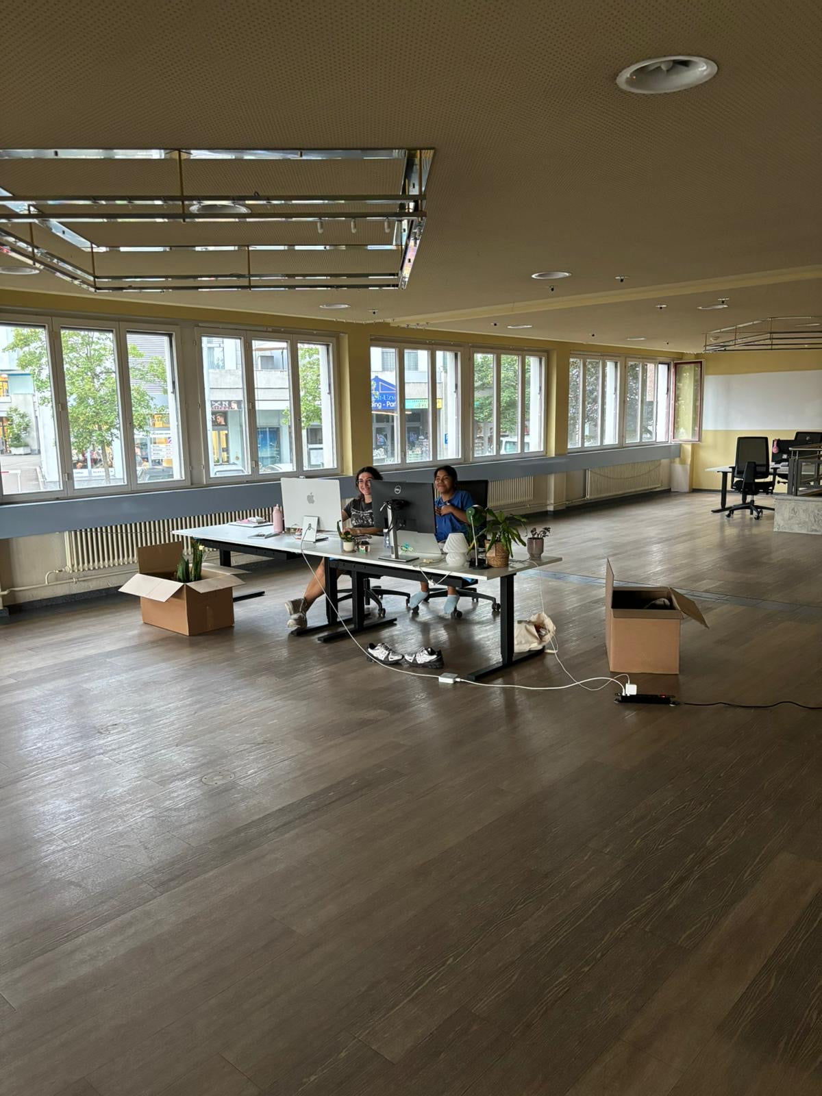 Zwei Frauen sitzen ganz alleine in einem grossen Raum an ihren Bürotischen.