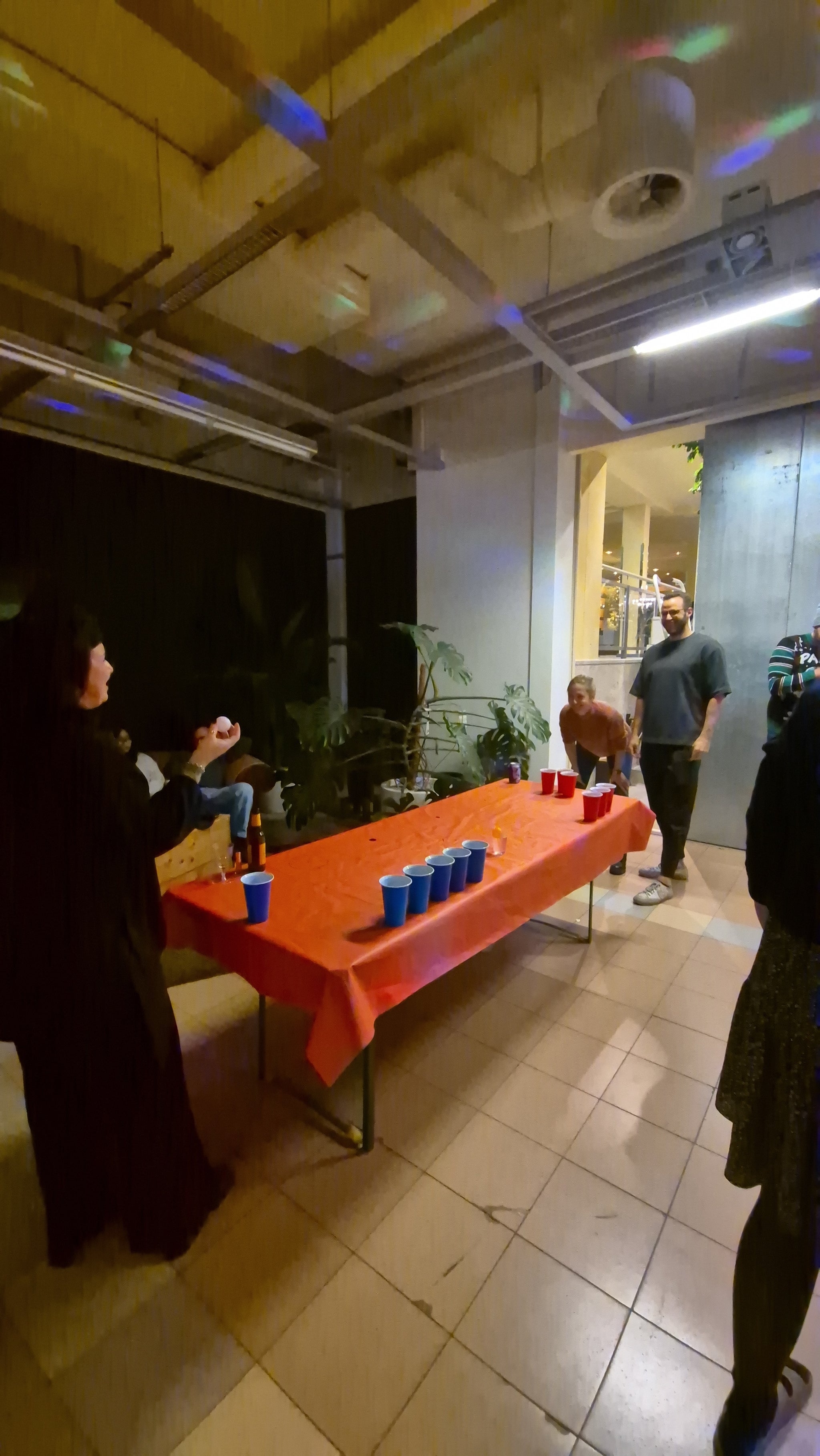Mehrere Personen spielen an einem länglichen Tisch Bierpong mit roten und blauen Becher.