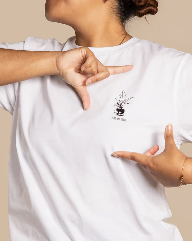 Eine Frau trägt ein weißes T-Shirt mit einem Bild einer Pflanze und der Aufschrift «Just one more».